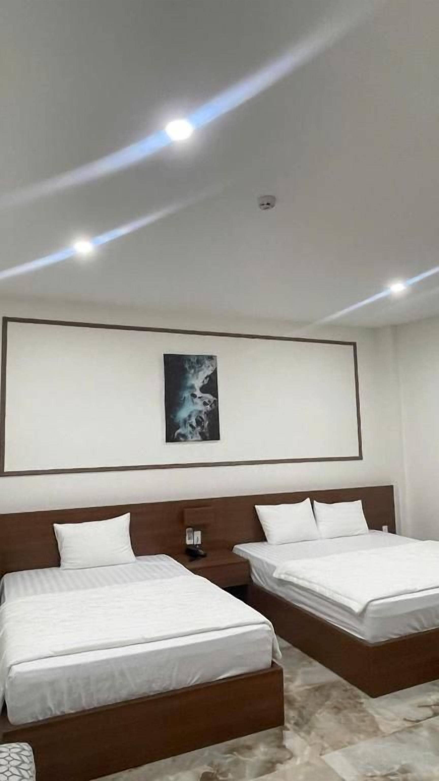 Habitación de hotel con dos camas, una mesita de noche y un diseño de techo moderno.