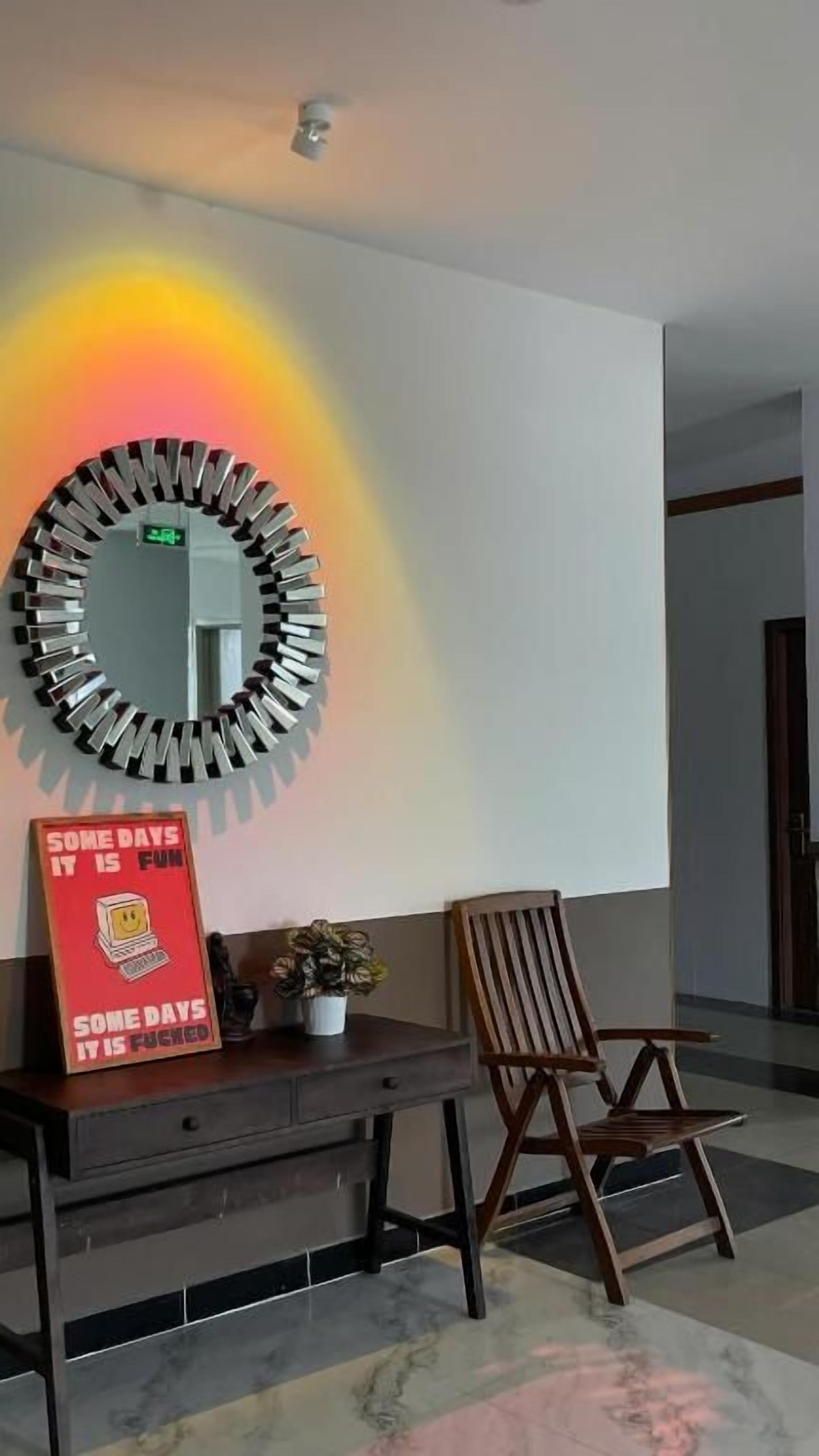 A room with a round mirror on the wall, a desk with a red sign, and a wooden chair.