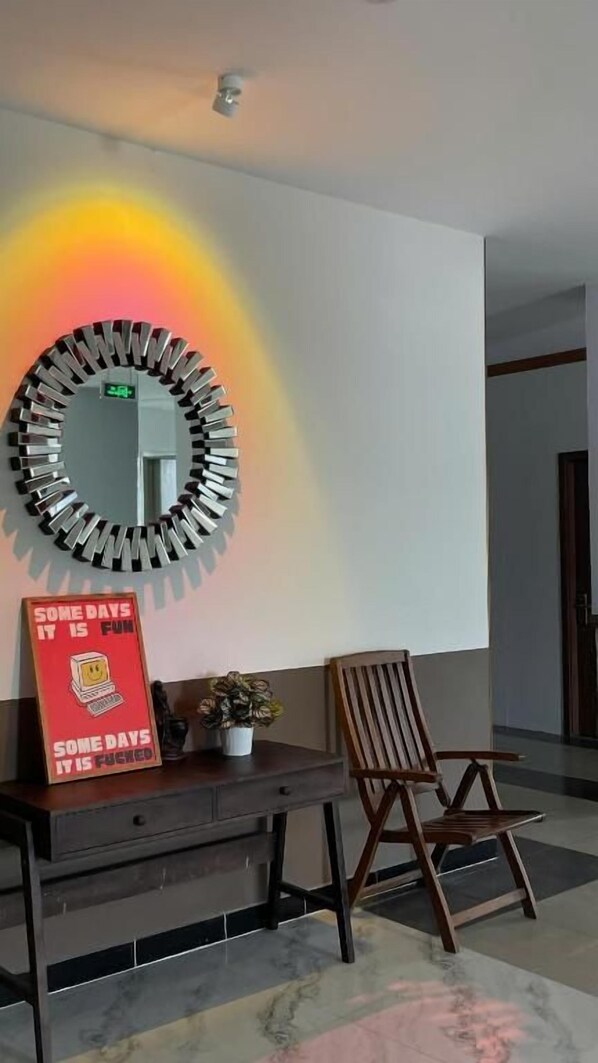 Una habitación con un espejo redondo en la pared, un escritorio con un letrero rojo y una silla de madera.