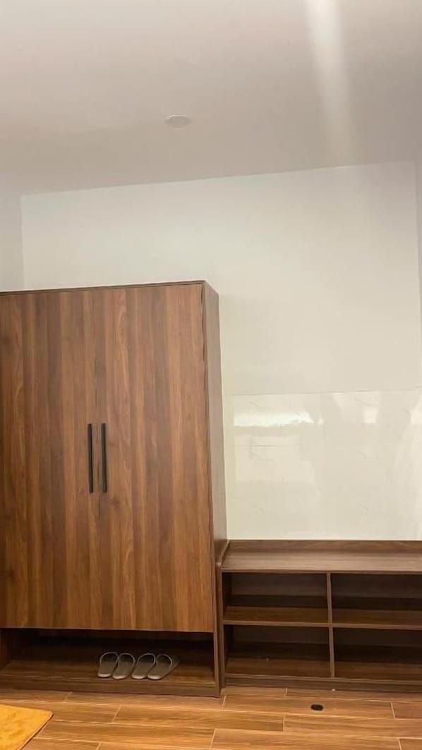 Une armoire en bois avec une porte miroir, un banc doté d’un espace de rangement en dessous, et une paire de chaussures posées sur le sol.