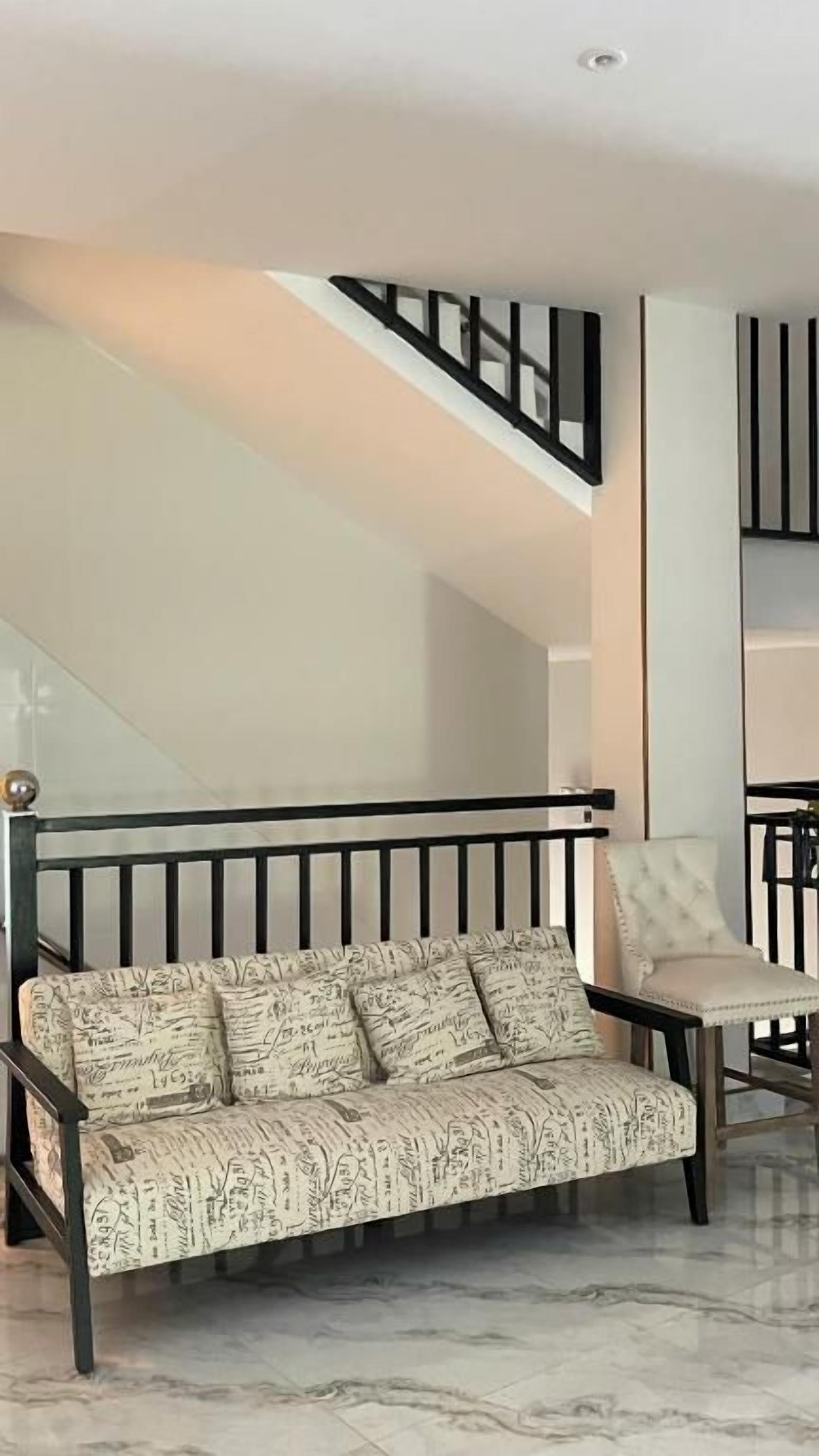 A modern living room with a sofa and armchair, a staircase, and a marble floor.