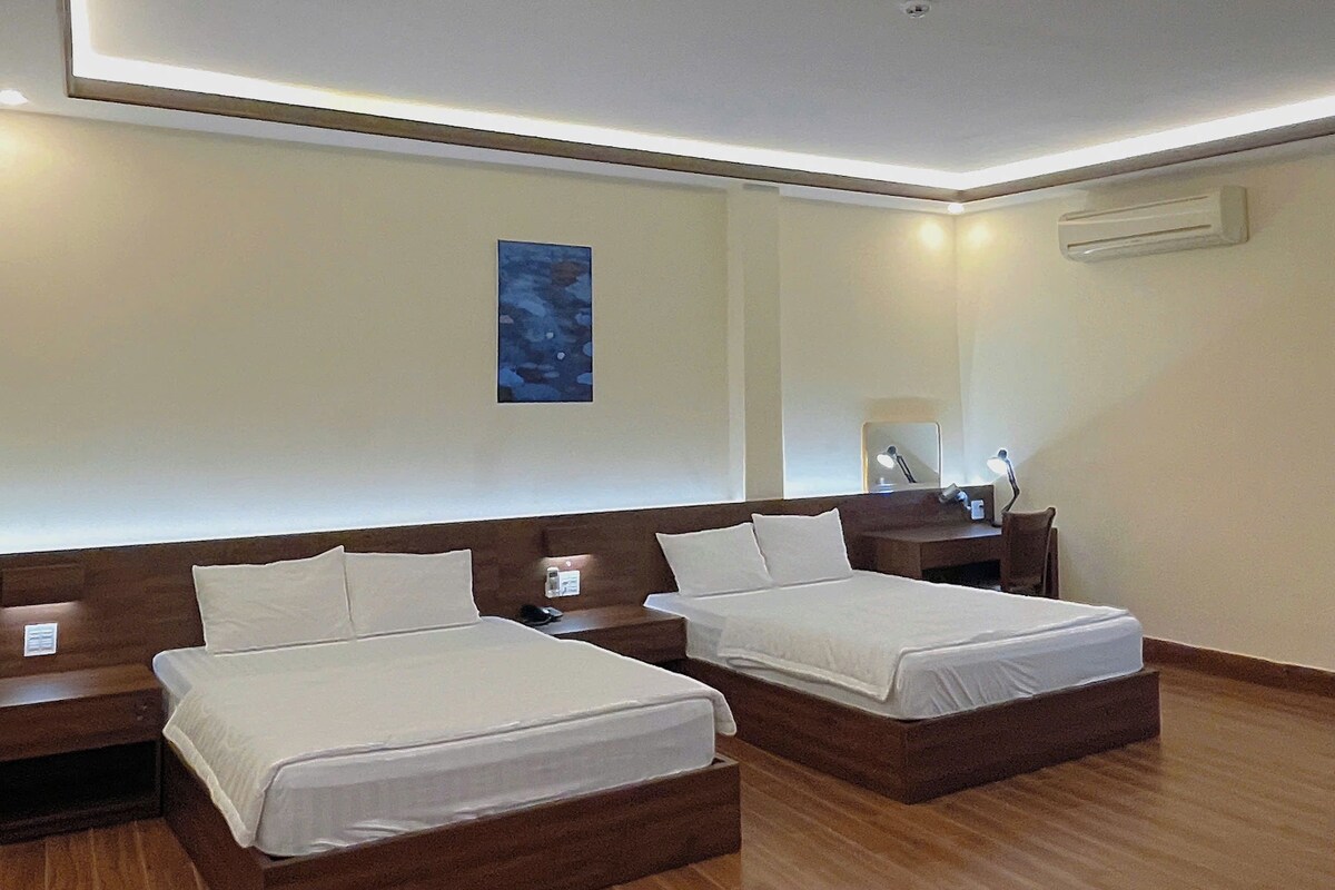Habitación de hotel con dos camas, una mesita de noche, aire acondicionado de pared y una lámpara del techo.