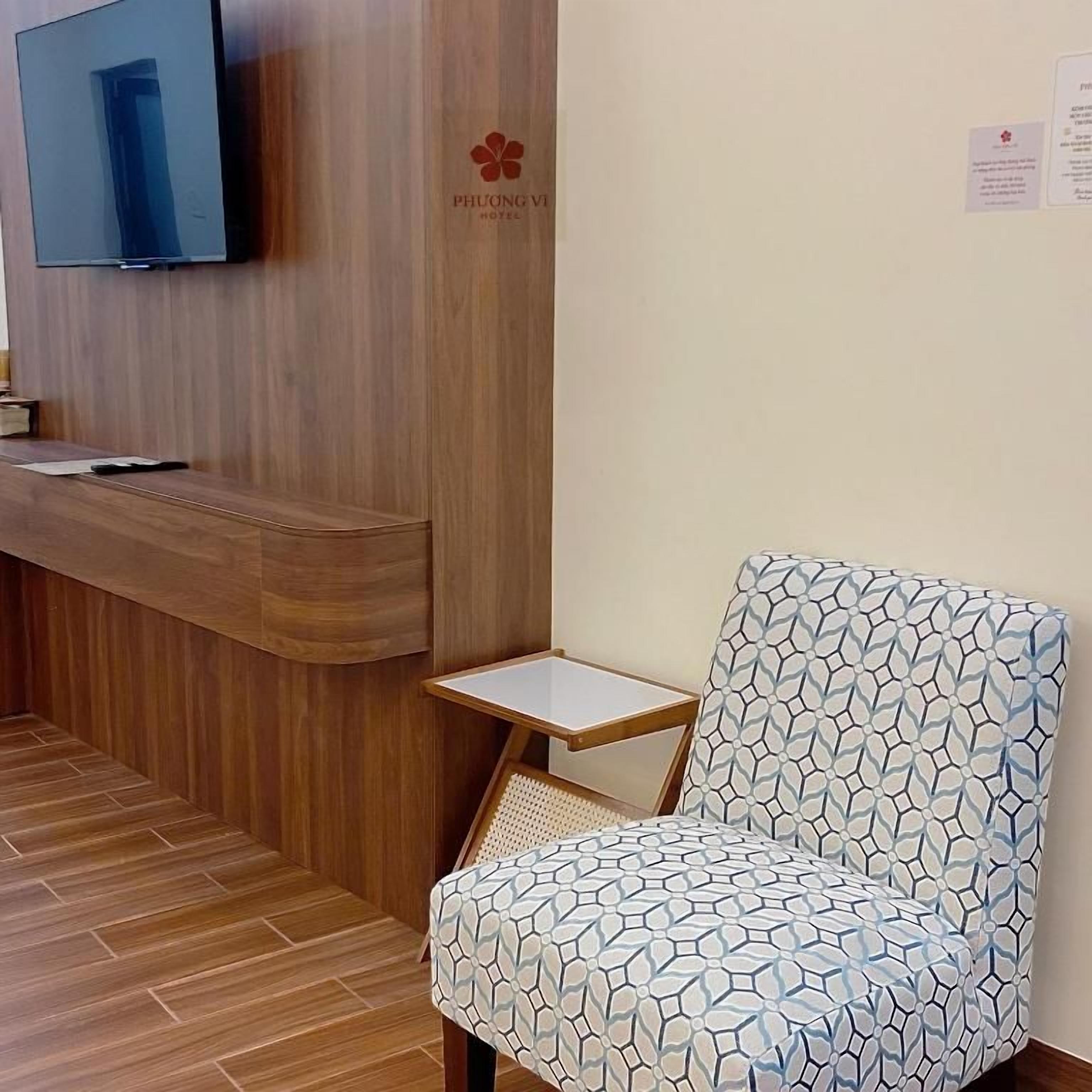 Zona de recepción de hotel con un mostrador de madera, un televisor montado en la pared y un sillón estampado.