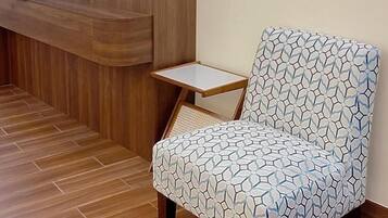 Zona de recepción de hotel con un mostrador de madera, un televisor montado en la pared y un sillón estampado.