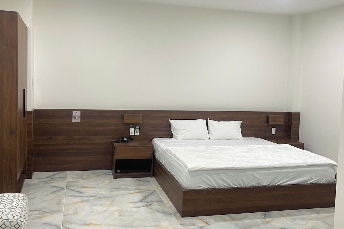 Un dormitorio con cabecera de madera, cama con ropa blanca, mesita de noche y una cómoda pequeña.