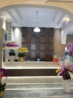 Zona de recepción con mostrador de mármol, plantas en macetas y un diseño de techo moderno.