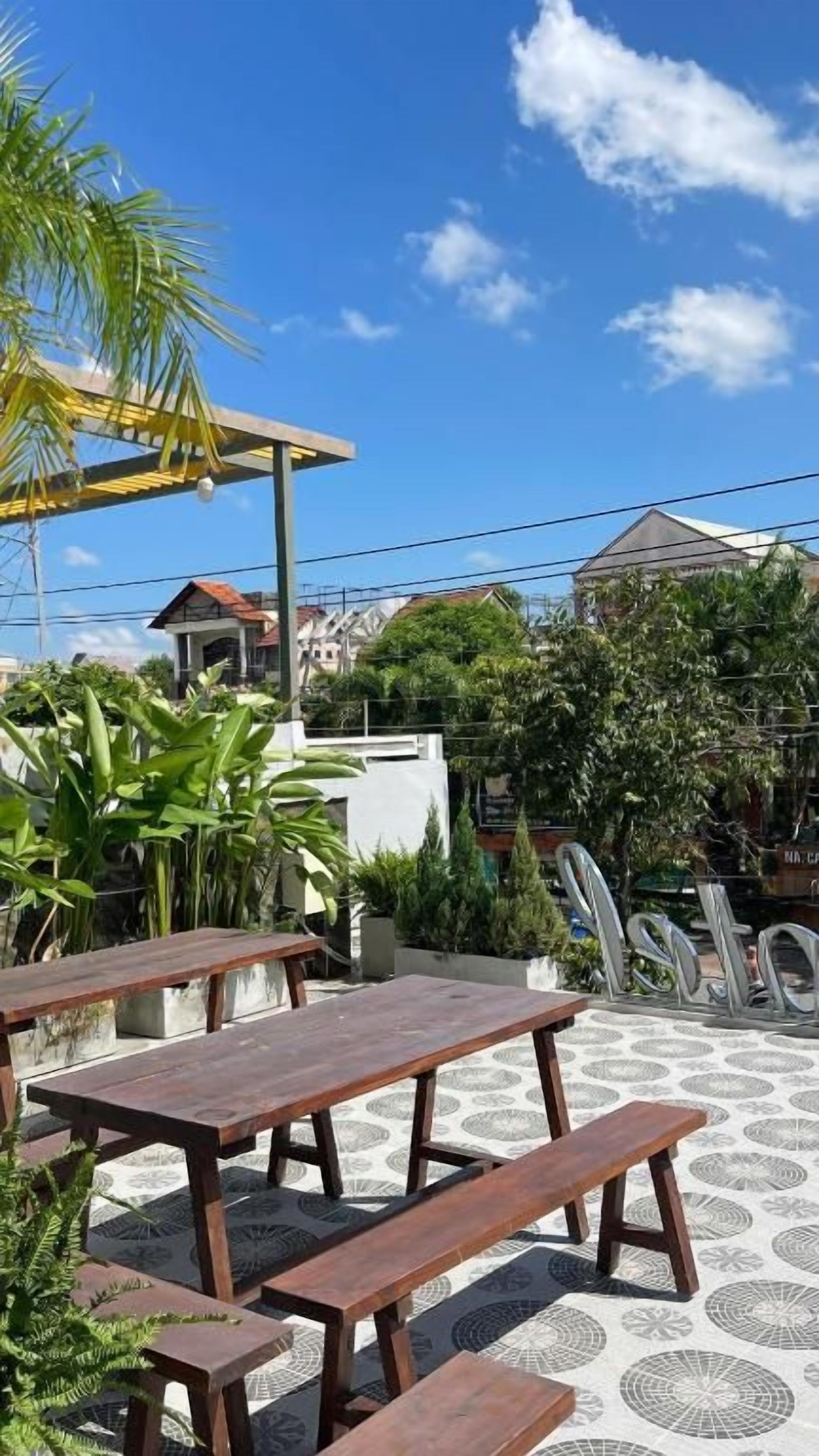 Une terrasse extérieure avec des tables et des bancs en bois, entourée de plantes en pot et dotée d’un sol à motifs.