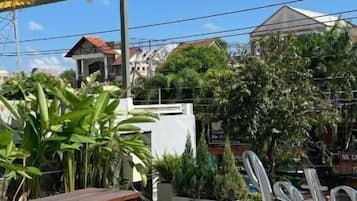Une terrasse extérieure avec des tables et des bancs en bois, entourée de plantes en pot et dotée d’un sol à motifs.