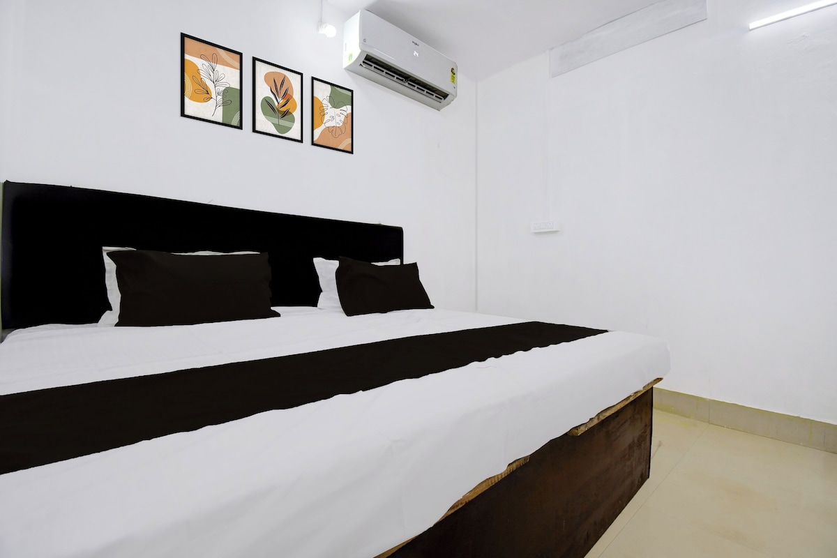 A bed with a black headboard, white bedding, and two black pillows. There are three framed pictures on the wall above the bed.