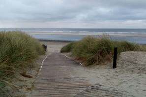 Ein Holzweg, der zu einem Strand mit Dünen an beiden Seiten führt.