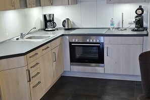 Eine kompakte Küche mit integriertem Backofen, einer Kaffeemaschine und einem Wasserkocher auf der Arbeitsfläche.