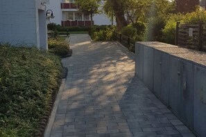 A paved pathway leading to a building with a red and white facade, surrounded by greenery and a metal fence. - Holiday apartment with 2 bedrooms (Langeoog)