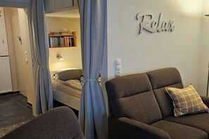 A bedroom with a bed, a nightstand, a lamp, a wardrobe, and a wall with the word 'Relax' on it. - Holiday apartment with 2 bedrooms (Langeoog)
