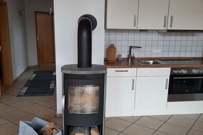 Une cuisine équipée d’un poêle à bois, de meubles blancs, d’un évier et d’un four.