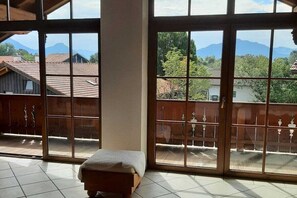 Une chambre avec un lit, de grandes fenêtres et une vue sur les montagnes et les maisons.