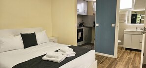 A hotel room with a bed, a nightstand, a bathroom with a sink and mirror, and a kitchenette. - Domingos Apartment (São Vicente)