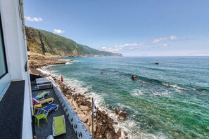 A balcony with colorful lounge chairs overlooking a rocky coastline and clear blue sea. - Domingos Apartment (São Vicente)
