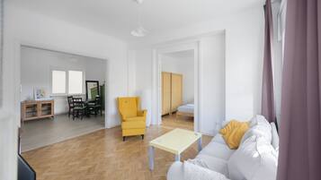 A spacious living area with a sofa, a yellow armchair, a small table, and a dining set.