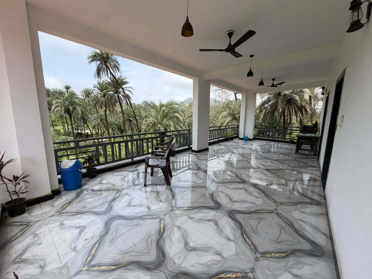 A covered outdoor area with a marble floor, ceiling fans, and a view of palm trees.