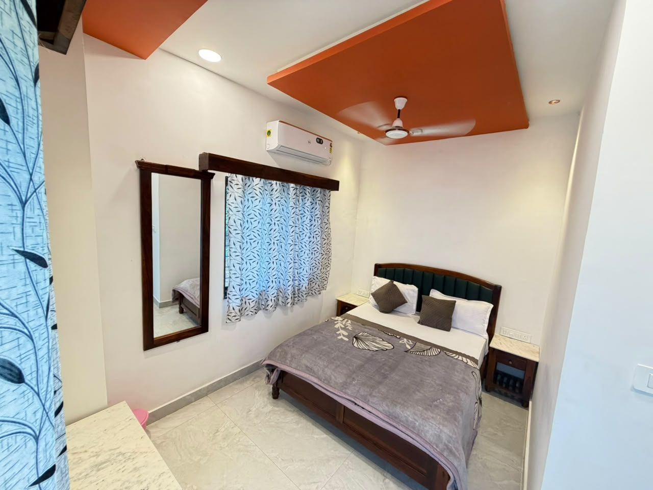 A bedroom with a bed, a nightstand, a mirror, an air conditioning unit, and a ceiling fan.