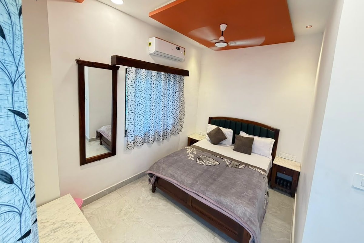 A bedroom with a bed, a nightstand, a mirror, an air conditioning unit, and a ceiling fan.