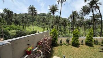 Varanda com vista para paisagem tropical, incluindo palmeiras e área gramada.
