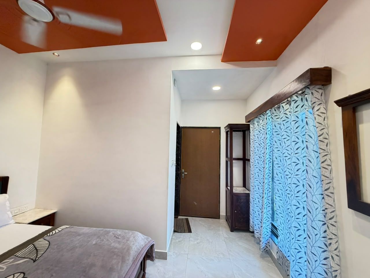 A hotel room with a bed, a wardrobe, a door, and a patterned curtain.