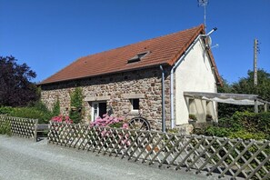 A stone building with a red-tiled roof, a wooden fence, and a wheelbarrow outside. - Holiday home in Vesly with swimming pool (Vesly)