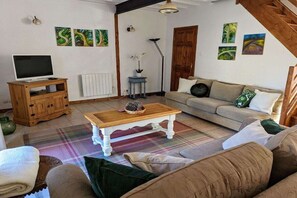 A living room with a sofa, a coffee table, a television on a wooden cabinet, and artwork on the walls. - Holiday home in Vesly with swimming pool (Vesly)