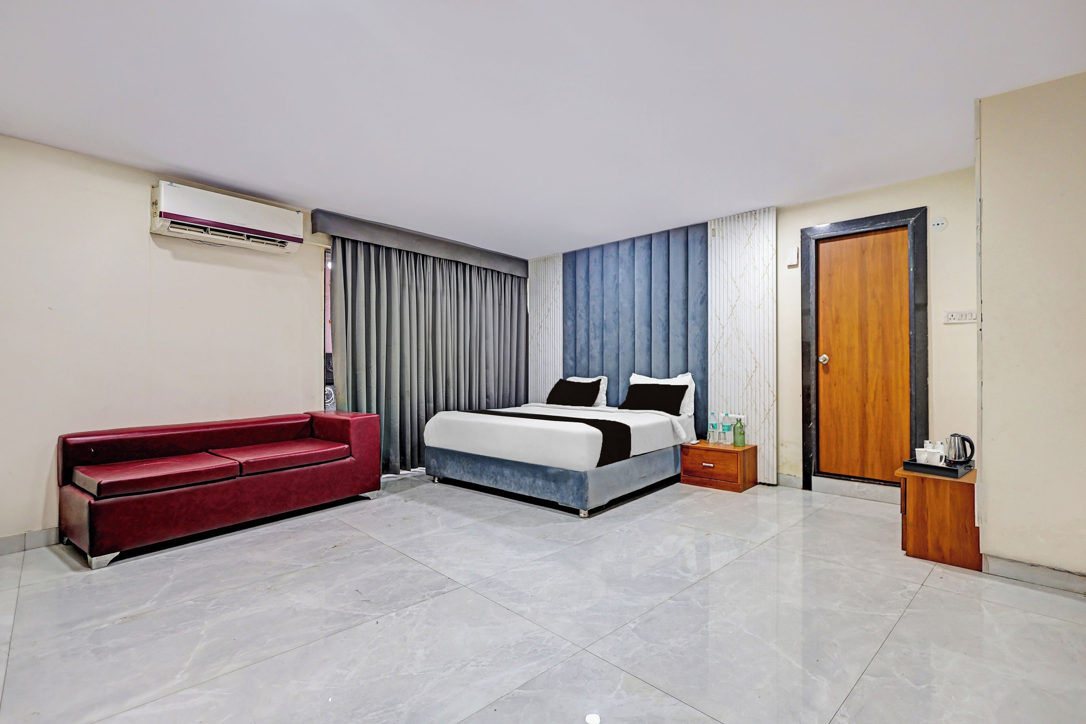 Una habitación de hotel con cama, sofá rojo, mesita de noche de madera y una puerta.