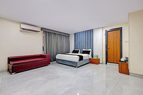 A hotel room with a bed, a red sofa, a wooden nightstand, and a door. - Townhouse Rau Circle (Indore)