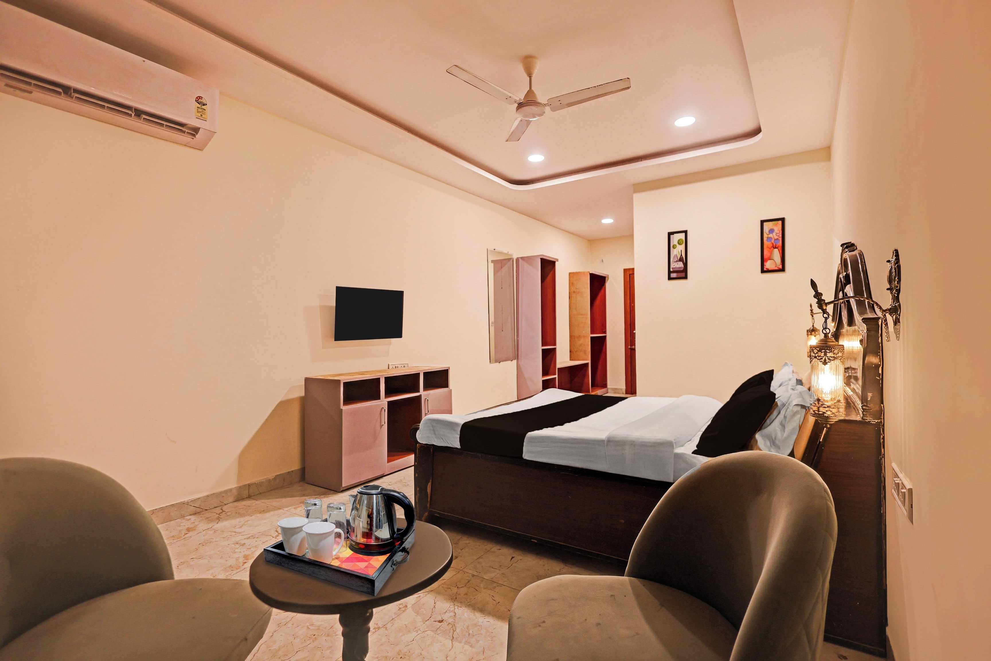 A hotel room with a bed, a TV, a desk, a chair, a coffee table, and a ceiling fan.