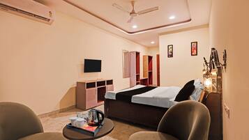 A hotel room with a bed, a TV, a desk, a chair, a coffee table, and a ceiling fan.