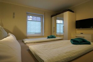 Une chambre d’hôtel avec deux lits, une télévision, une fenêtre avec des stores et un miroir au-dessus de la porte.