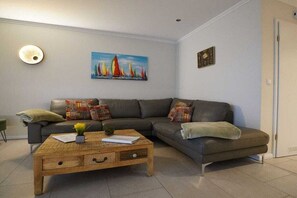 A living room with a sectional sofa, a wooden coffee table, and a painting on the wall. - Holiday apartment with 2 bedrooms (Norddeich)