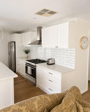 A modern kitchen with white cabinetry, a stainless steel range hood, a built-in oven, and a toaster. - Best of Both Beaches in Blairgowrie (Mornington Peninsula Shire)