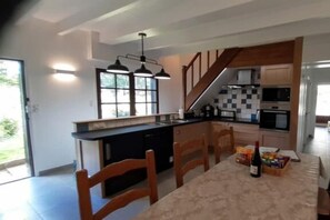 A modern kitchen with a central island, built-in appliances, and a dining area with wooden chairs. - Gite - Les Ravalieres (Livre-la-Touche)
