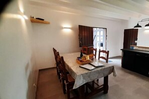 A dining area with a table set for four, a kitchen area with a counter and cabinets, and a door leading to an outdoor space. - Gite - Les Ravalieres (Livre-la-Touche)