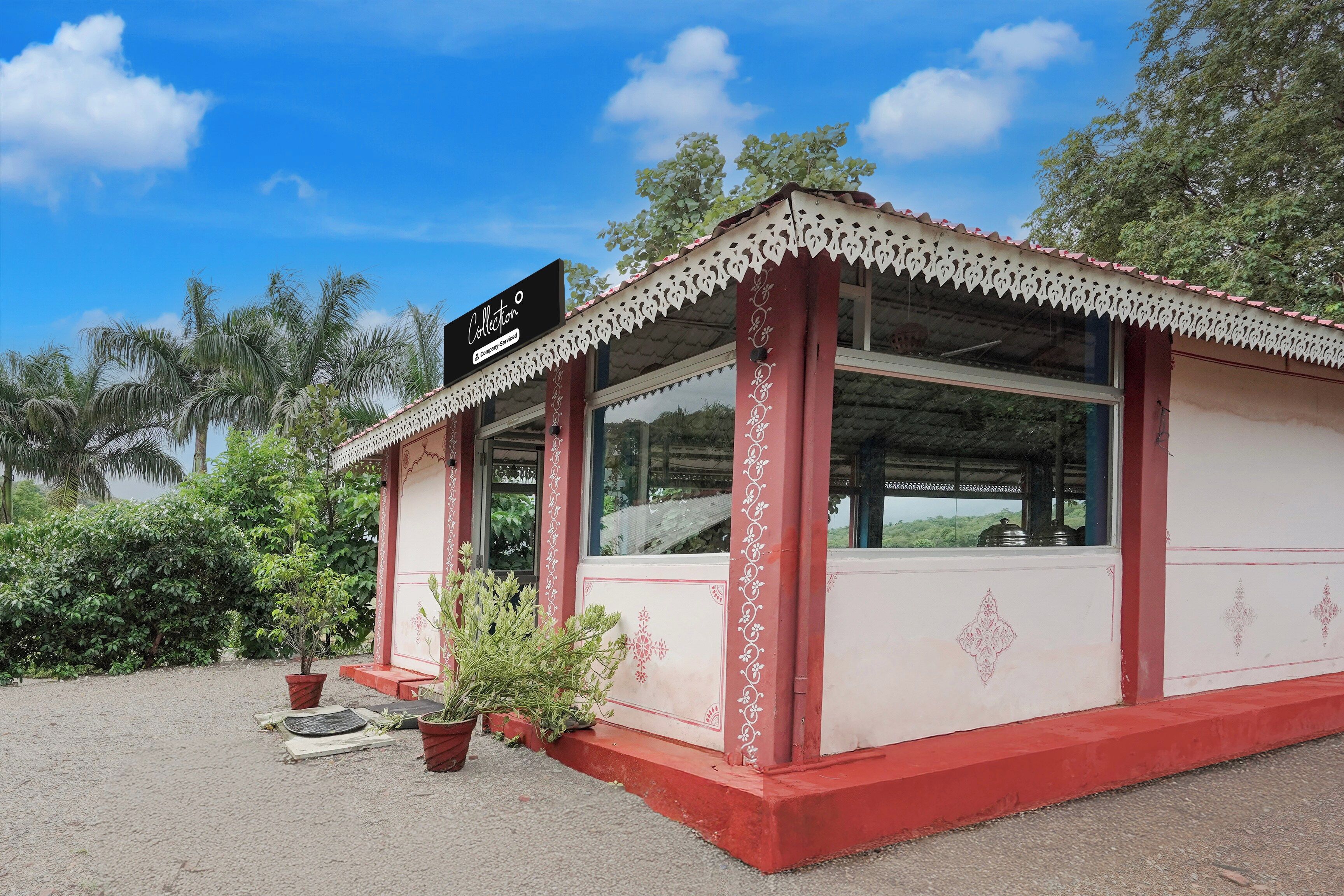 A small, single-story building with a red and white exterior, a sign indicating it is a company-serviced location, and a window with a view of the surrounding greenery.