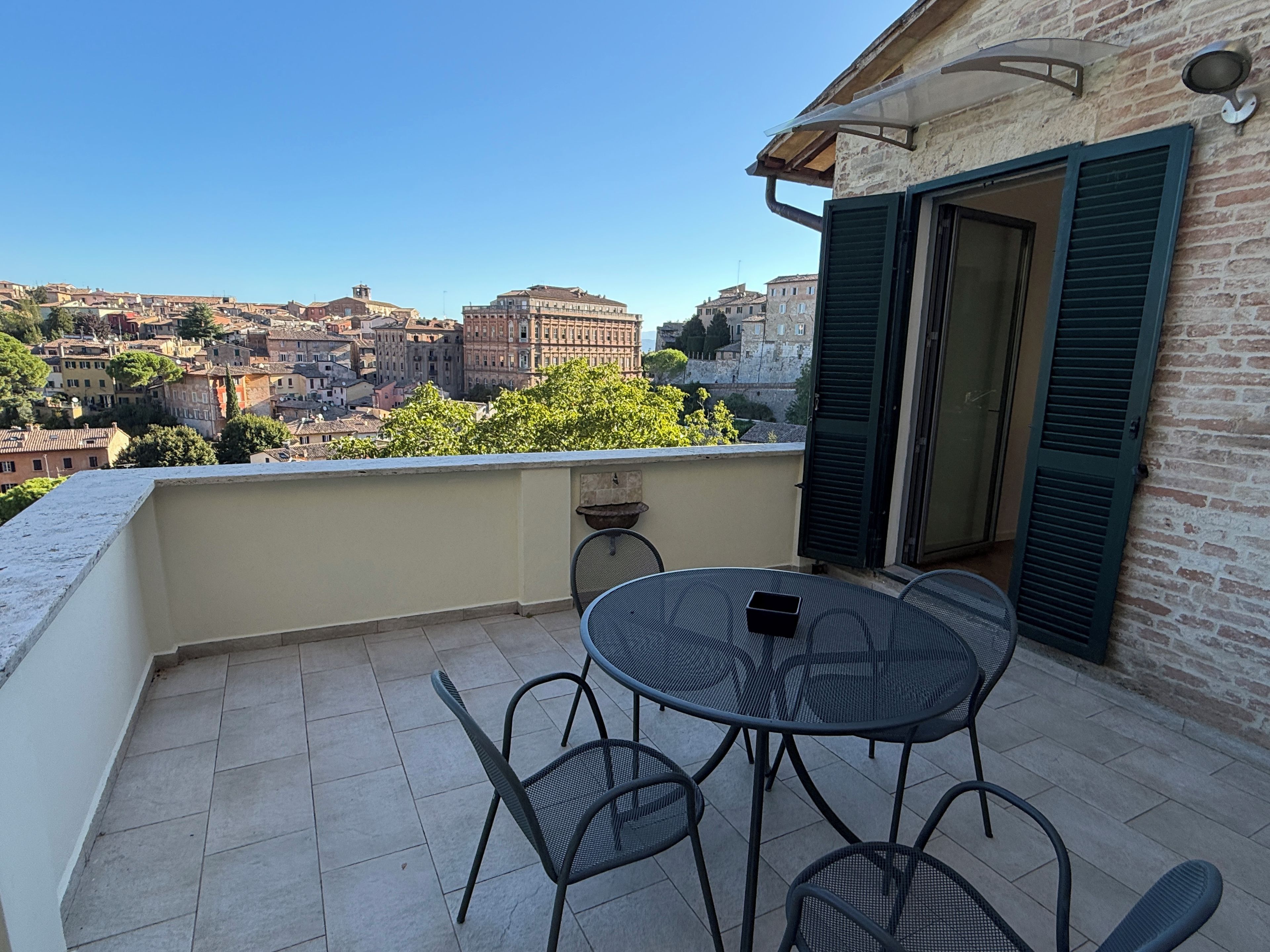 A balcony with a table and chairs, overlooking a cityscape with historic buildings.