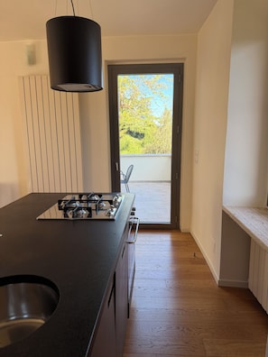 A modern kitchen with a central island, a black pendant light, and a view through an open door to an outdoor balcony. - Historic residence in the city center (Perugia)