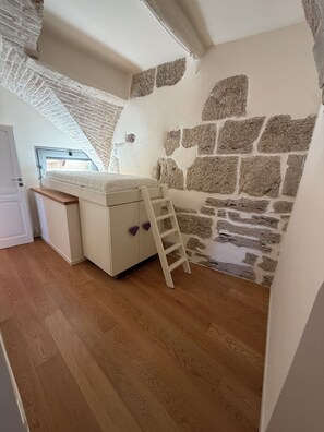 A bedroom with a loft bed, a wooden ladder, and a stone wall. - Historic residence in the city center (Perugia)
