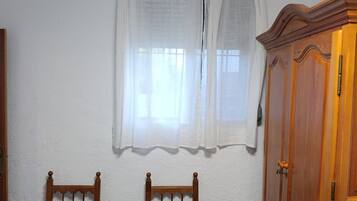 A room with two wooden chairs, a wooden wardrobe, and a window with sheer curtains.