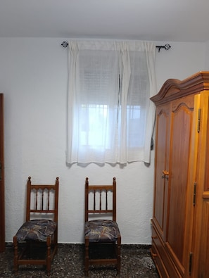 Una habitació amb dues cadires de fusta, un armari de fusta i una finestra amb cortines transparents.