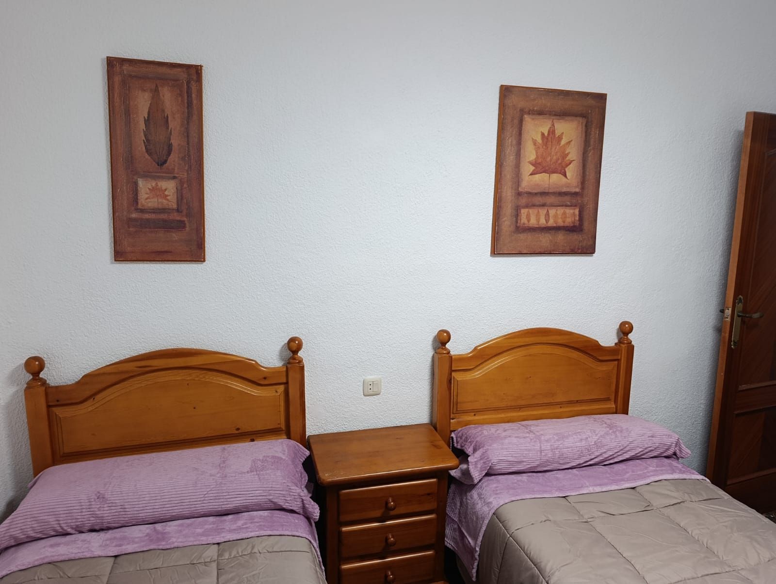 A room with two wooden beds, a nightstand, a dresser, and two framed pictures on the wall.