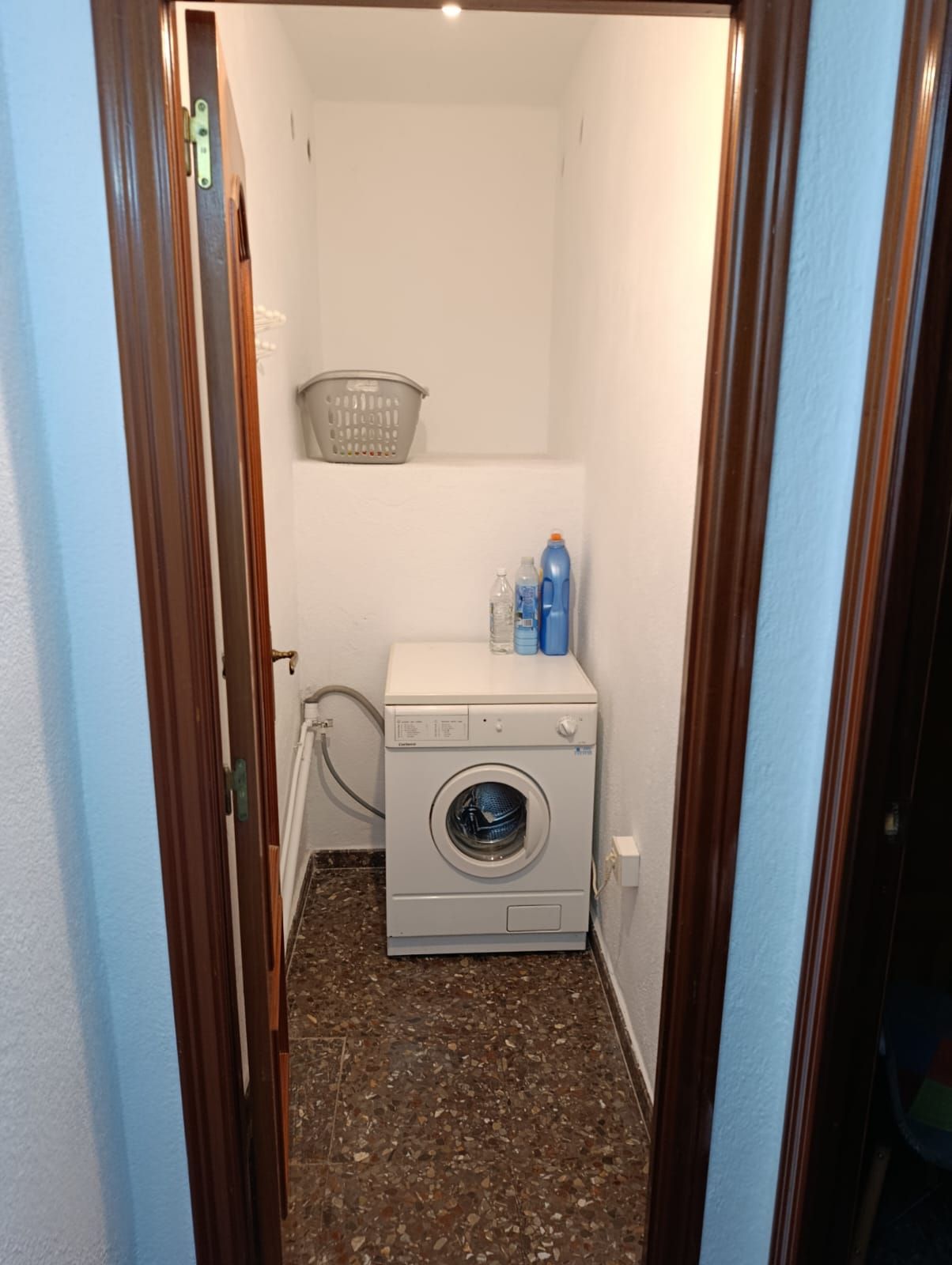 A laundry room with a washing machine, a basket, and detergent bottles.