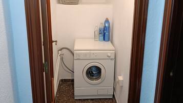 A laundry room with a washing machine, a basket, and detergent bottles.