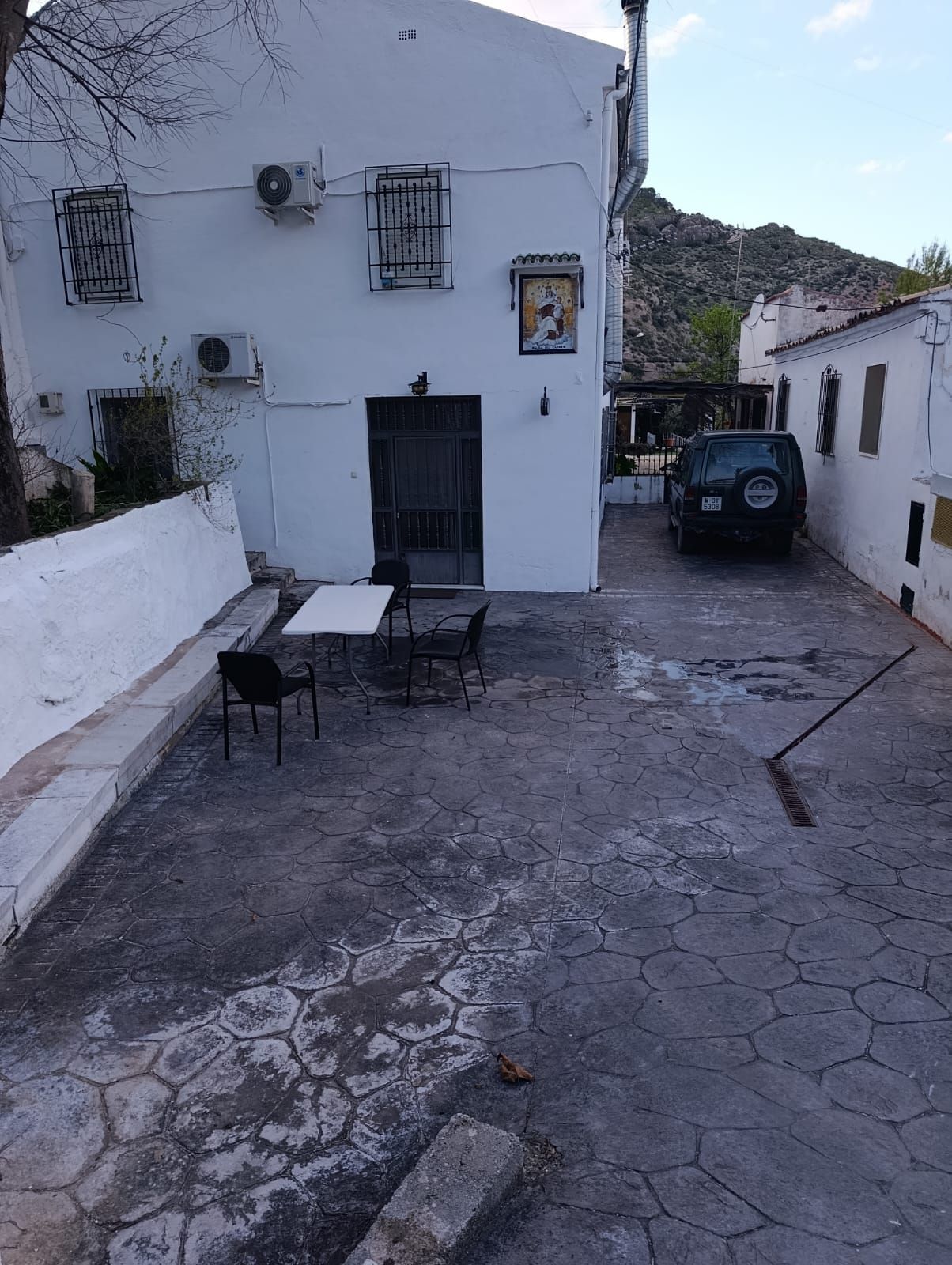 A courtyard with a white building, a table with chairs, and a parked car.