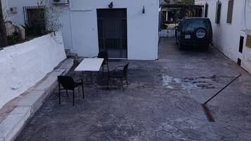 A courtyard with a white building, a table with chairs, and a parked car.