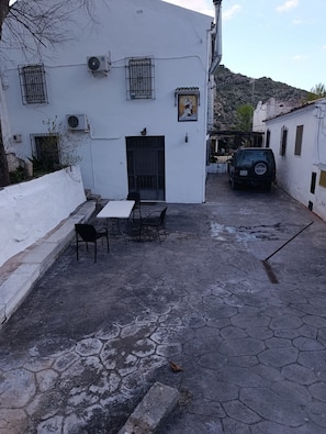 Un pati amb un edifici blanc, una taula amb caires i un cotxe aparcat.